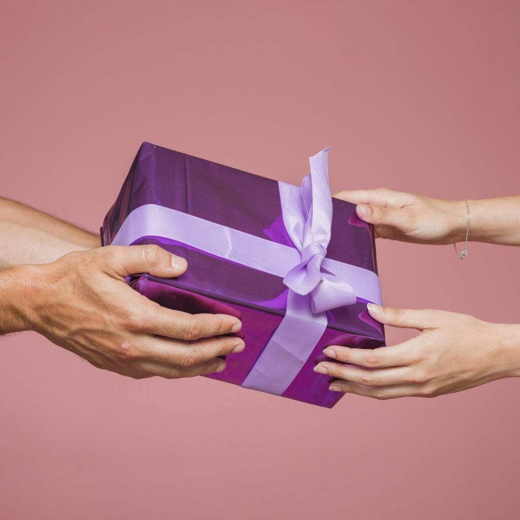close up two hands holding purple gift boxes against colored background